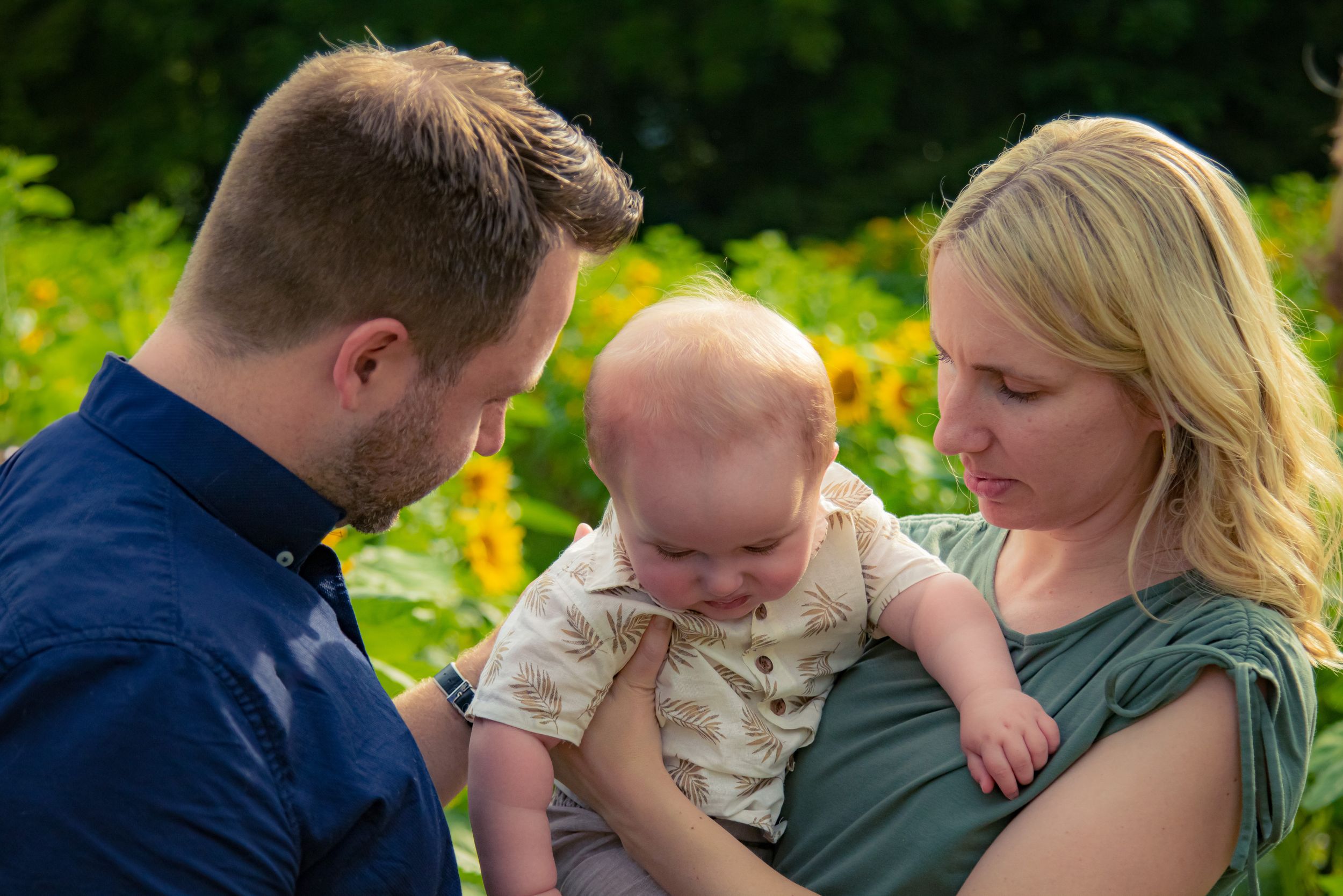 A family shares tender moments together in a series of outdoor portraits set against a lush green background.