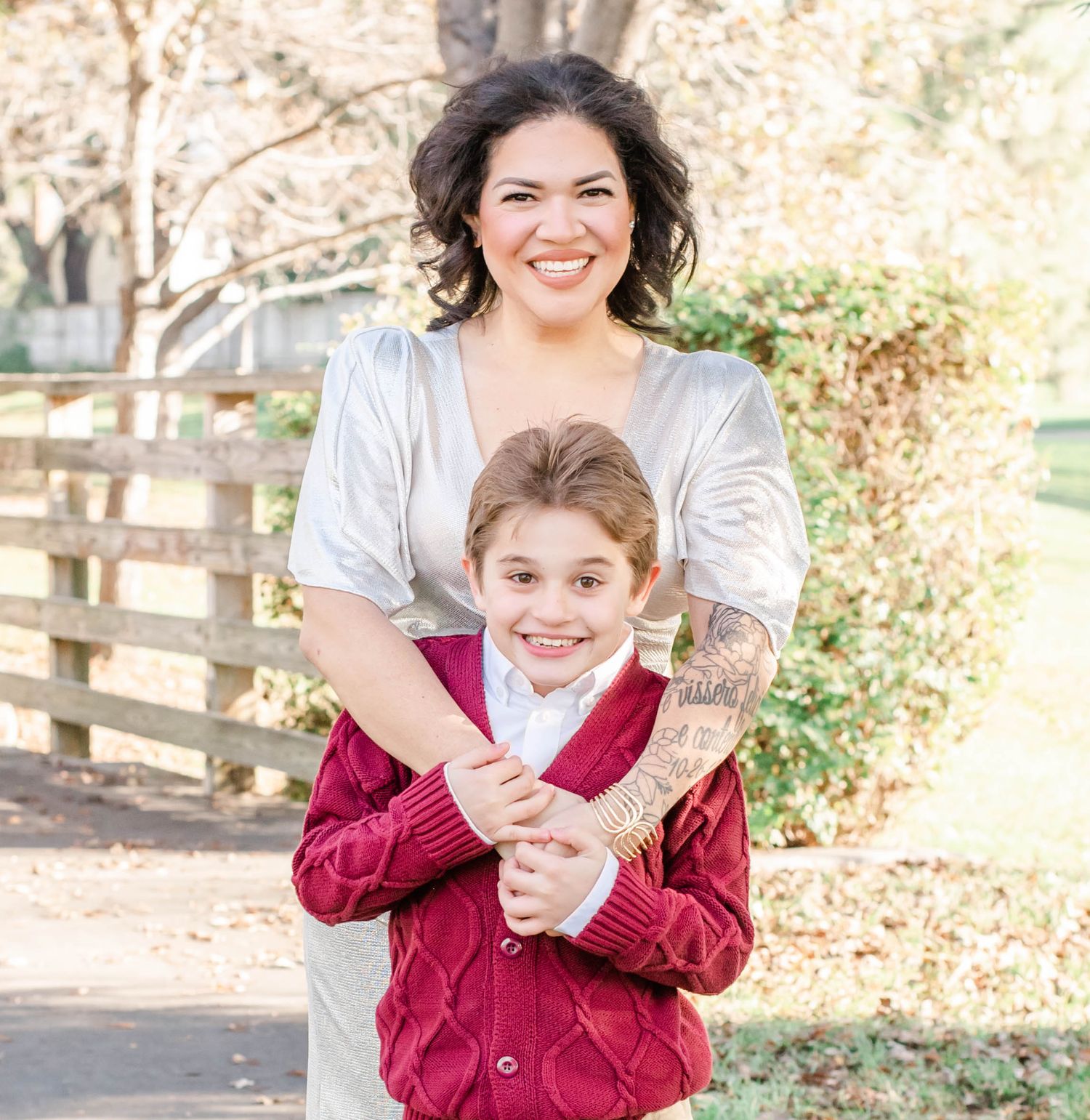 A family wearing burgundy and white outfits poses playfully together in a rustic outdoor setting during autumn.