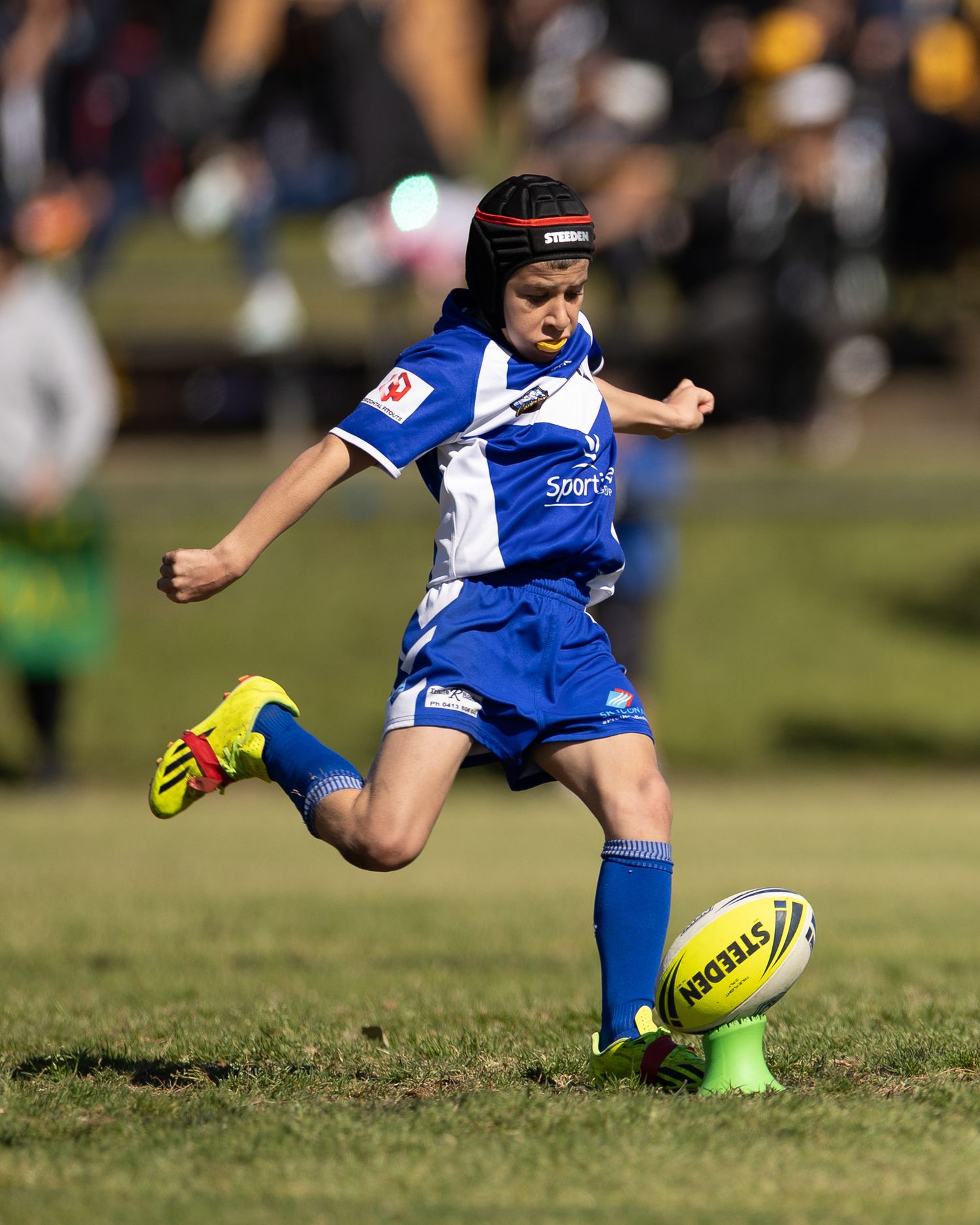 Soccer player in blue and white jersey kicks ball during match on grass field.