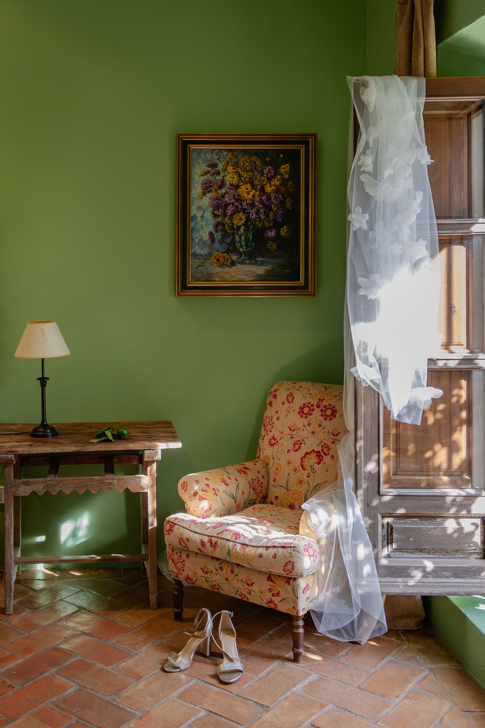 Elegant room with green walls, floral couch, and sheer white curtains filtering sunlight.