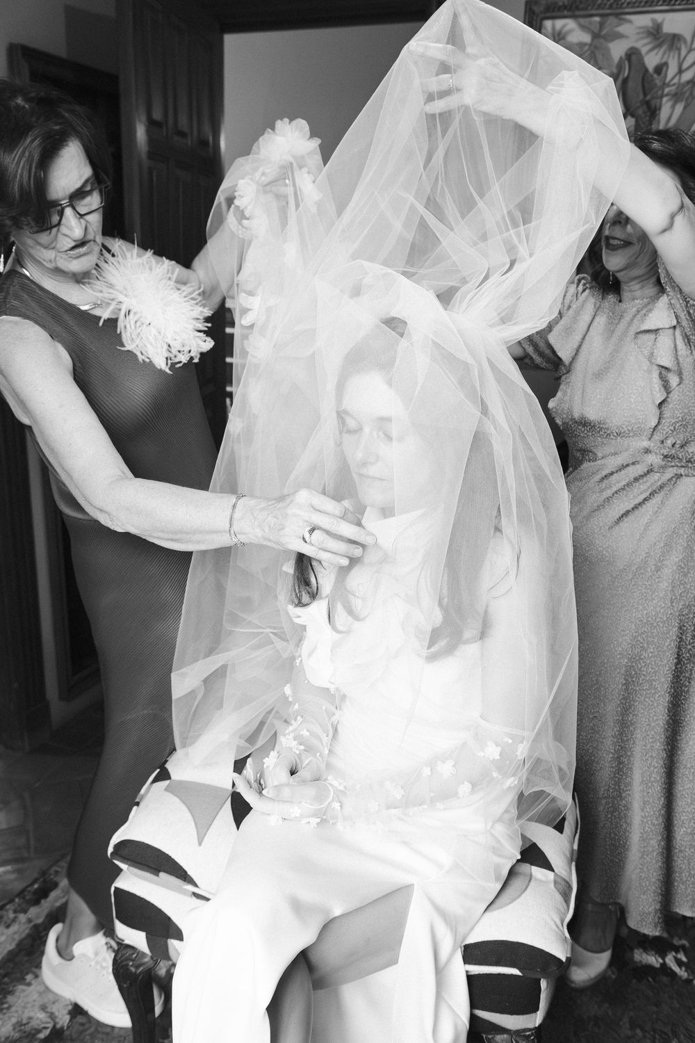 A series of black and white photos showing a bride getting dressed in her wedding gown and veil.