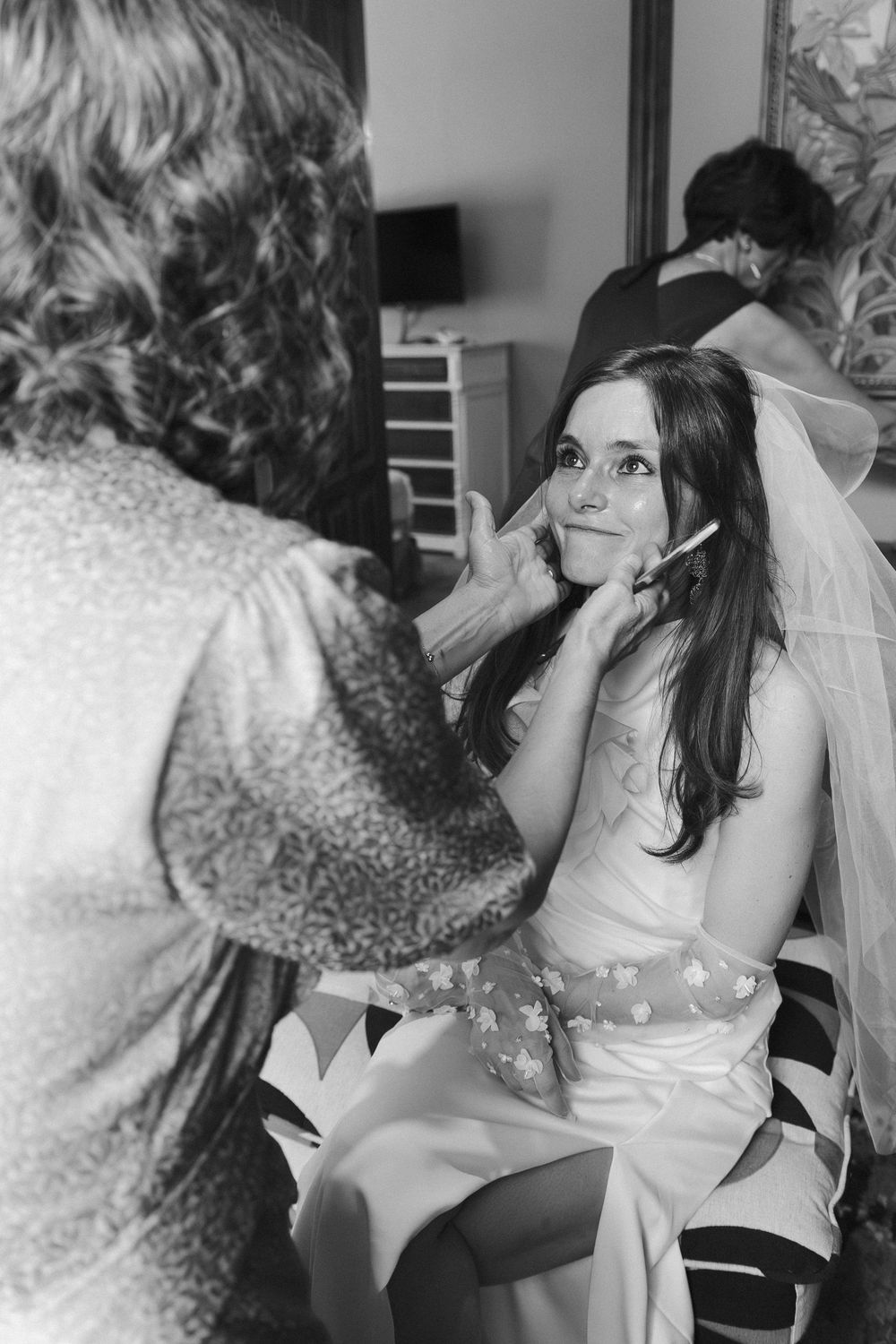 A candid black and white photo captures preparation moments with makeup application.