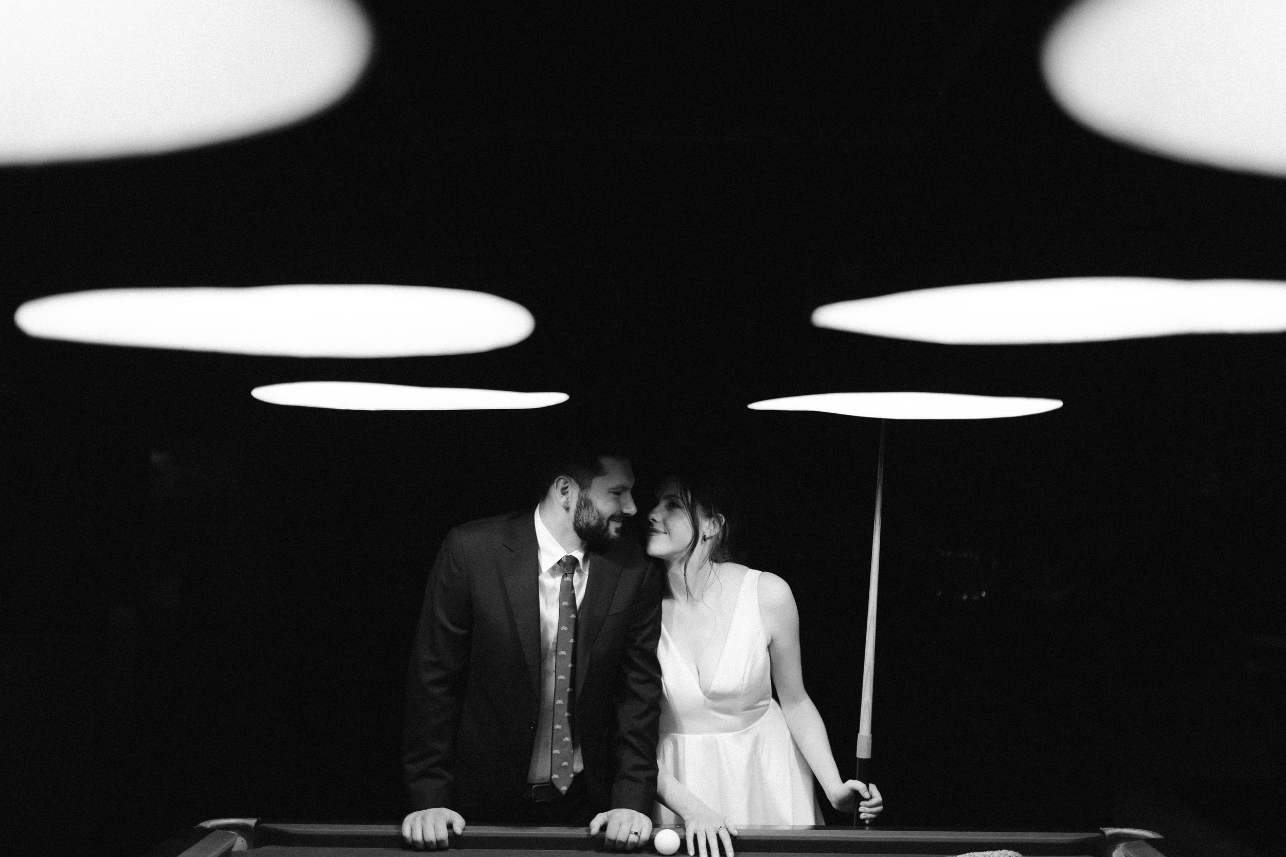 Dramatic black and white wedding reception scene with overhead lighting.