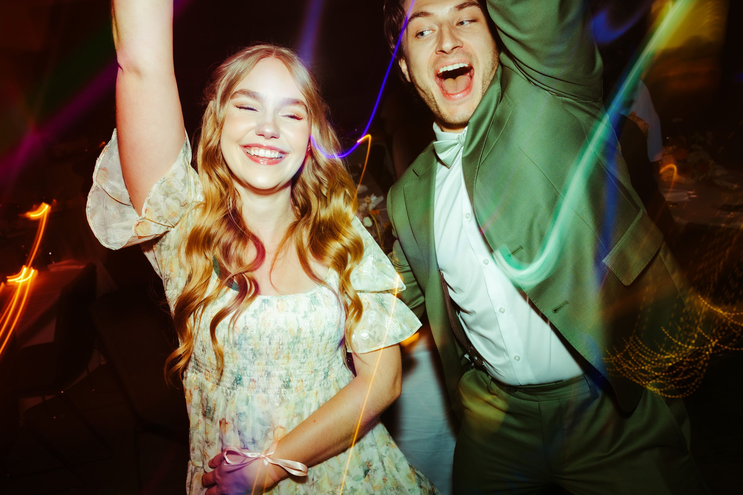 Energetic dancing and celebration at a wedding reception with colorful lighting.