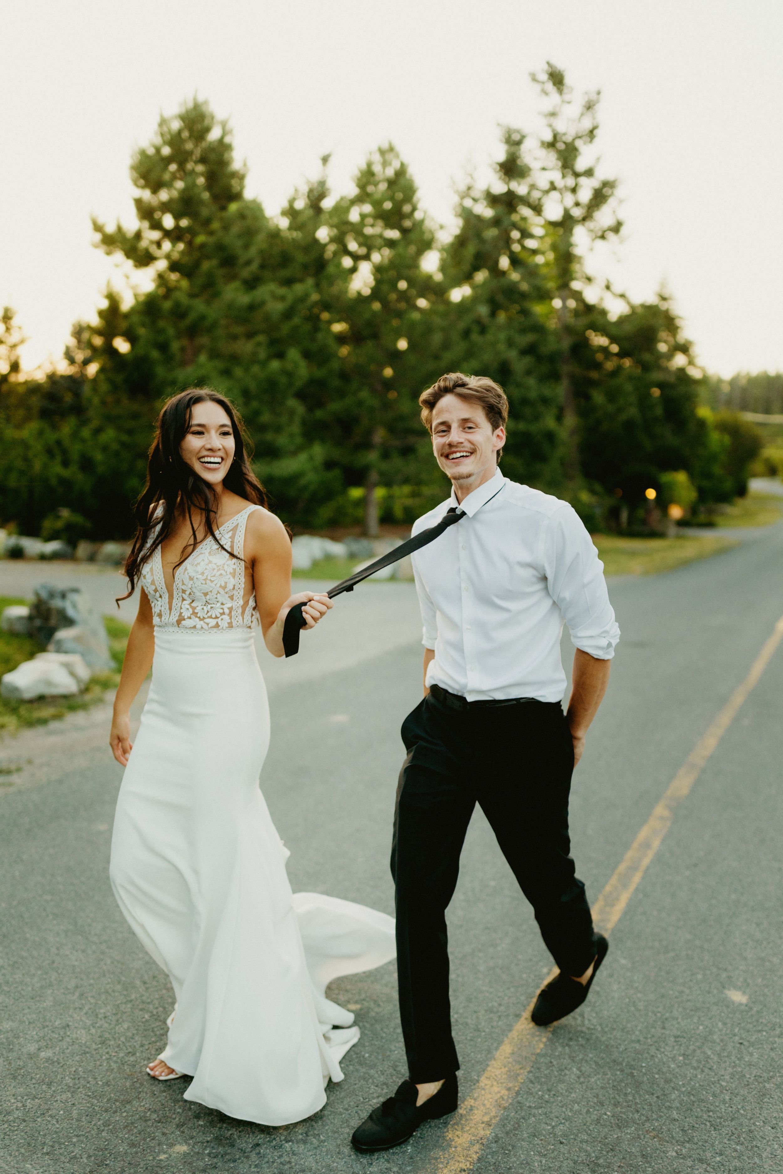 Playful wedding couple dances and poses on an empty road at sunset.