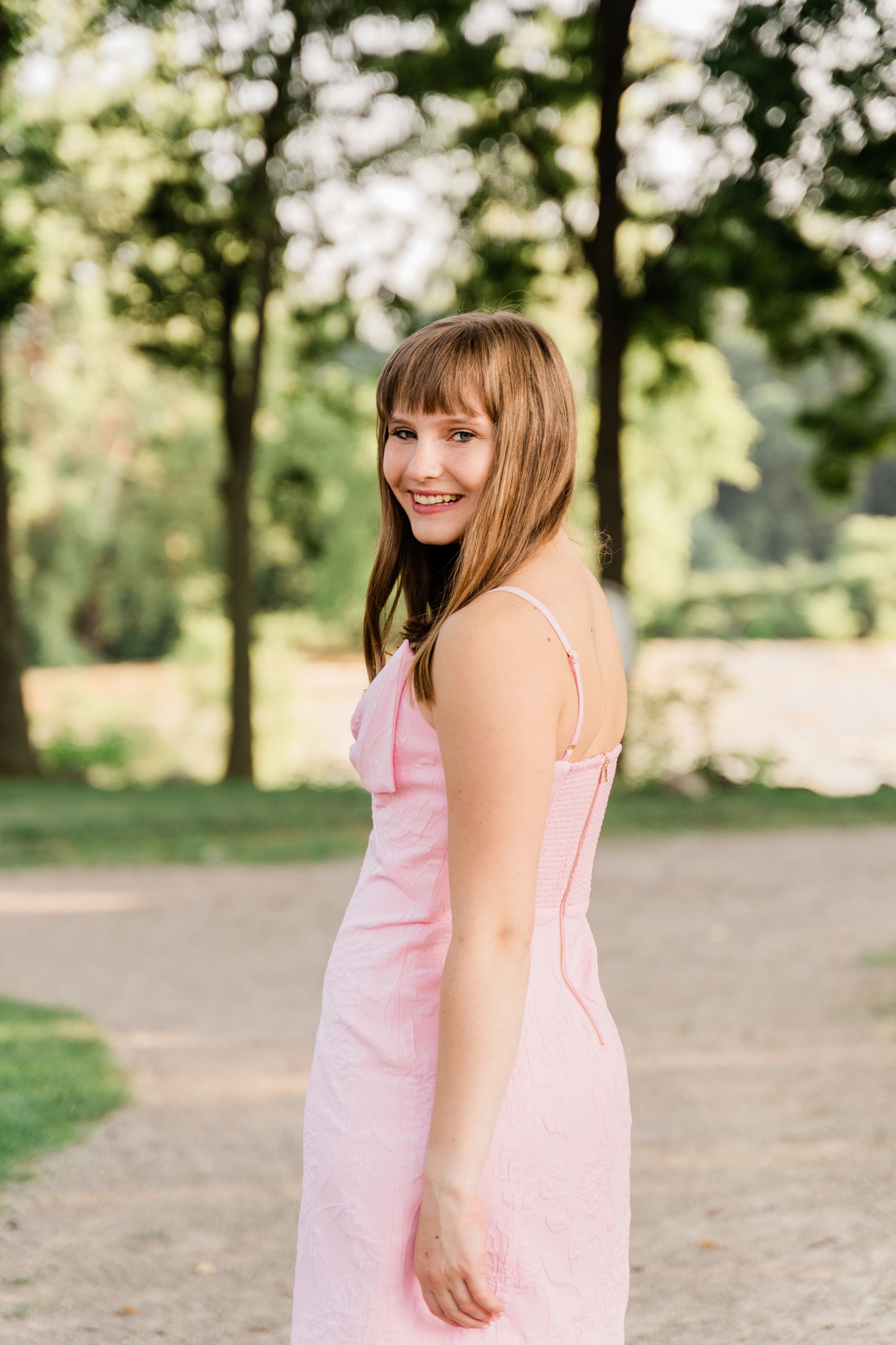 A series of outdoor portraits in a park setting featuring a pink summer dress and natural sunlit backdrop.