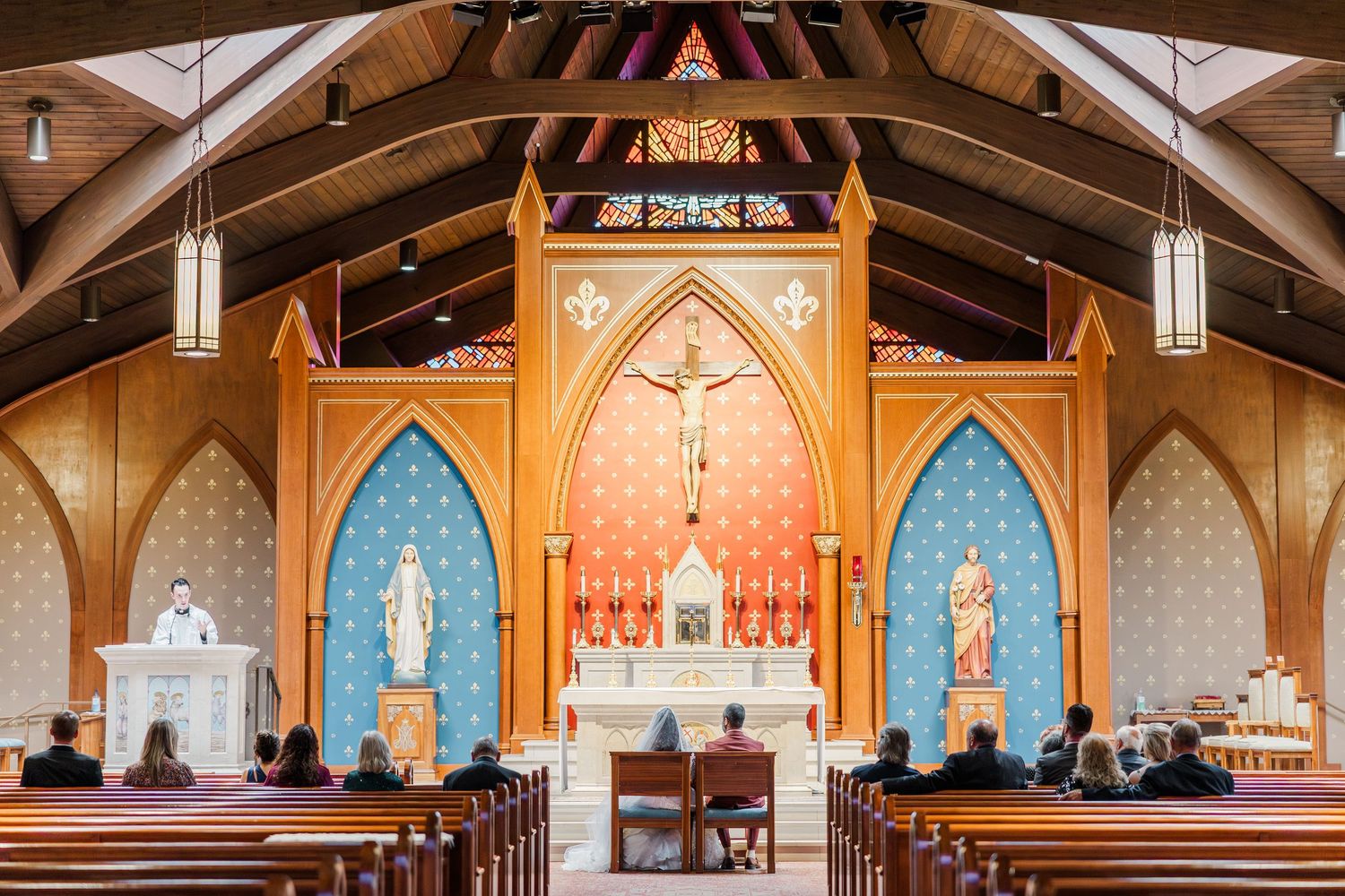Interior view of a Catholic church sanctuary with wooden beams, blue arched niches, and a central golden altar.