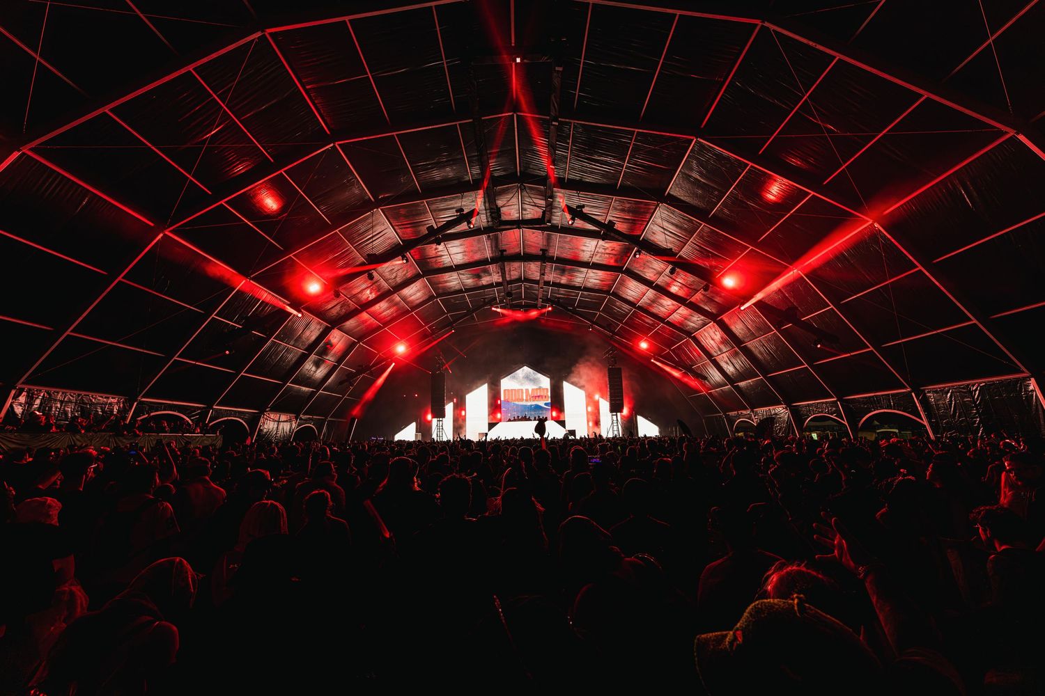 Concert arena illuminated with dramatic red lighting and laser effects during a live performance.