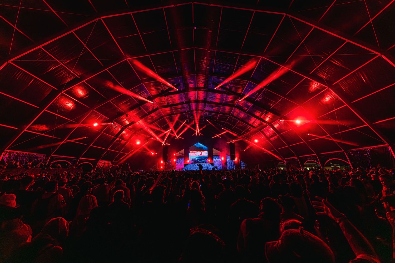 Red laser lights illuminate a dark concert venue with a curved ceiling creating a dramatic atmosphere during a performance.