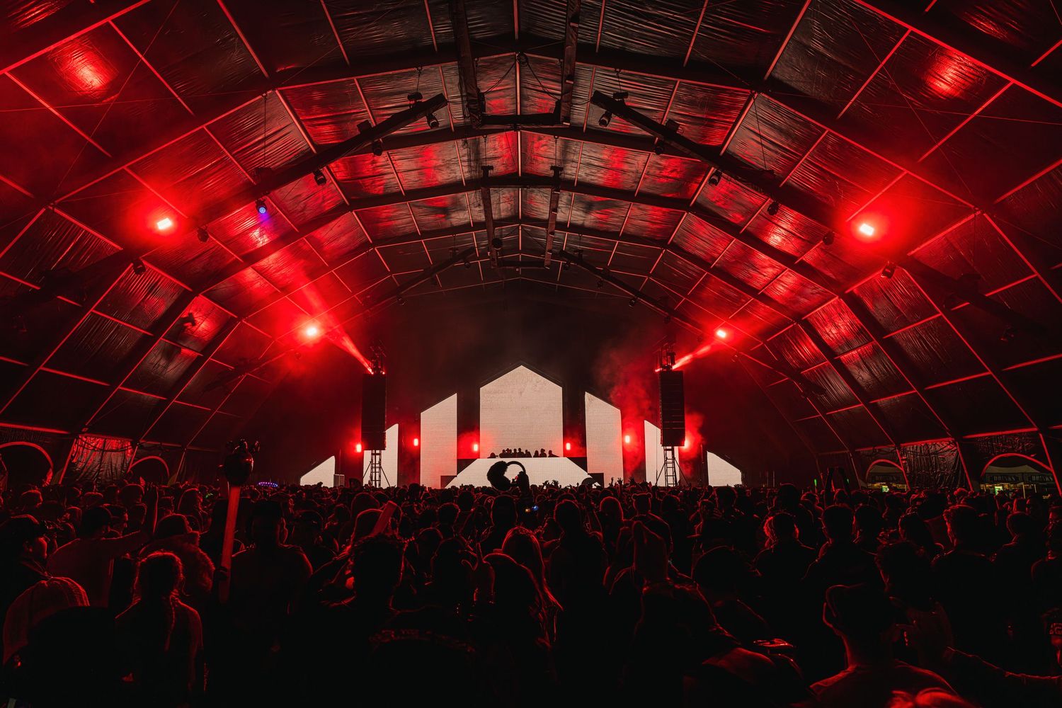 Concert venue illuminated with dramatic red lighting and arched ceiling structure creates an atmospheric performance space.