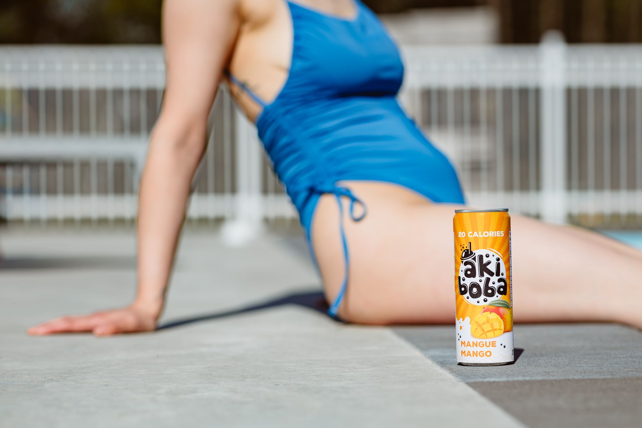 Can of orange soda placed on poolside ledge next to someone in blue swimwear.