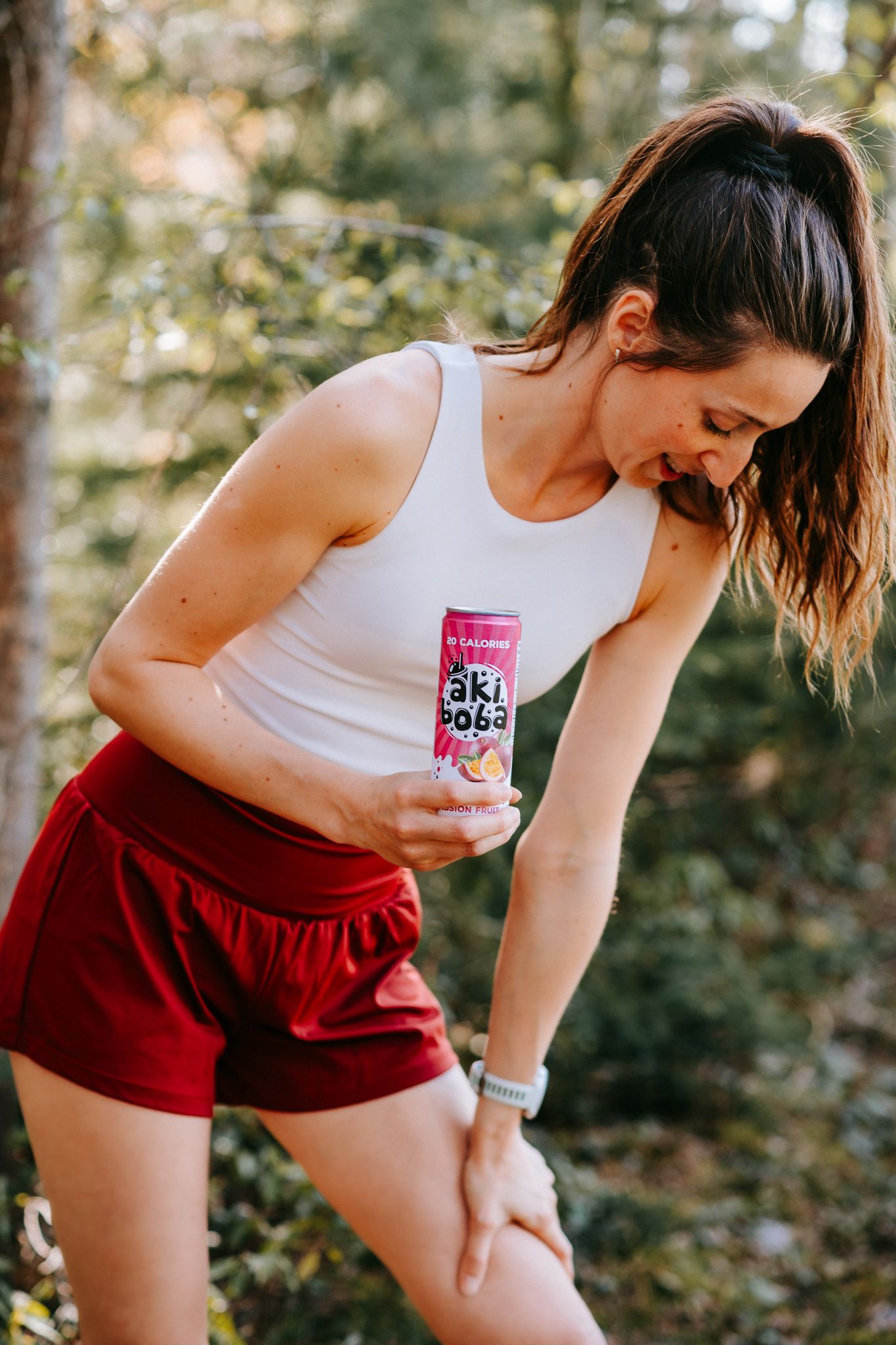 Athletic outfit with red shorts and white tank top paired with canned beverage in forest setting.