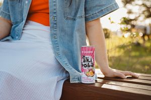 Close-up view of someone wearing denim jacket sitting at outdoor bench with Oki Poki drink.