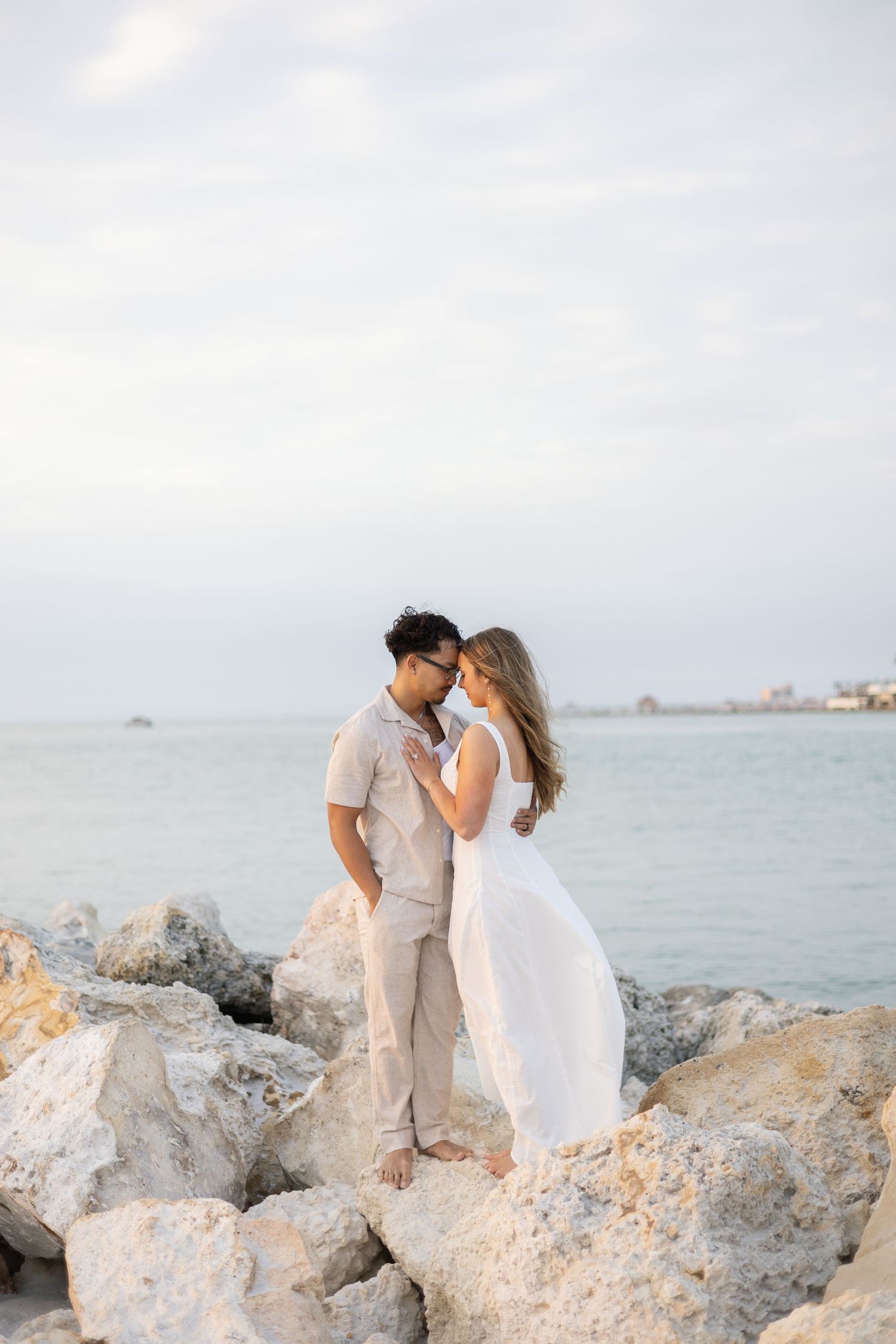 A couple walks together on a sandy beach path lined with sea grape trees during golden hour.