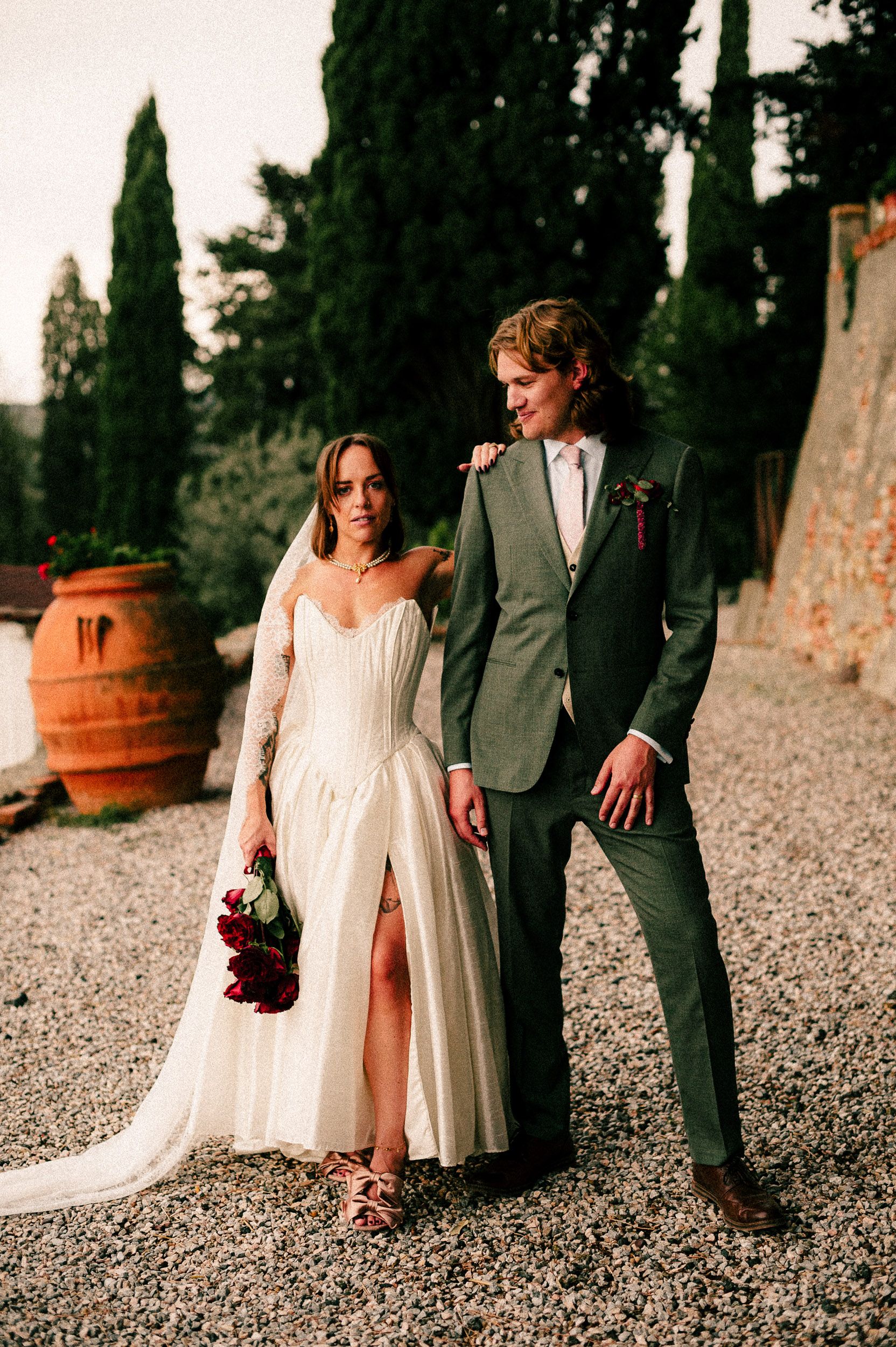A couple walks together on a gravel path, the bride wearing a flowing white dress and the groom in a gray suit.