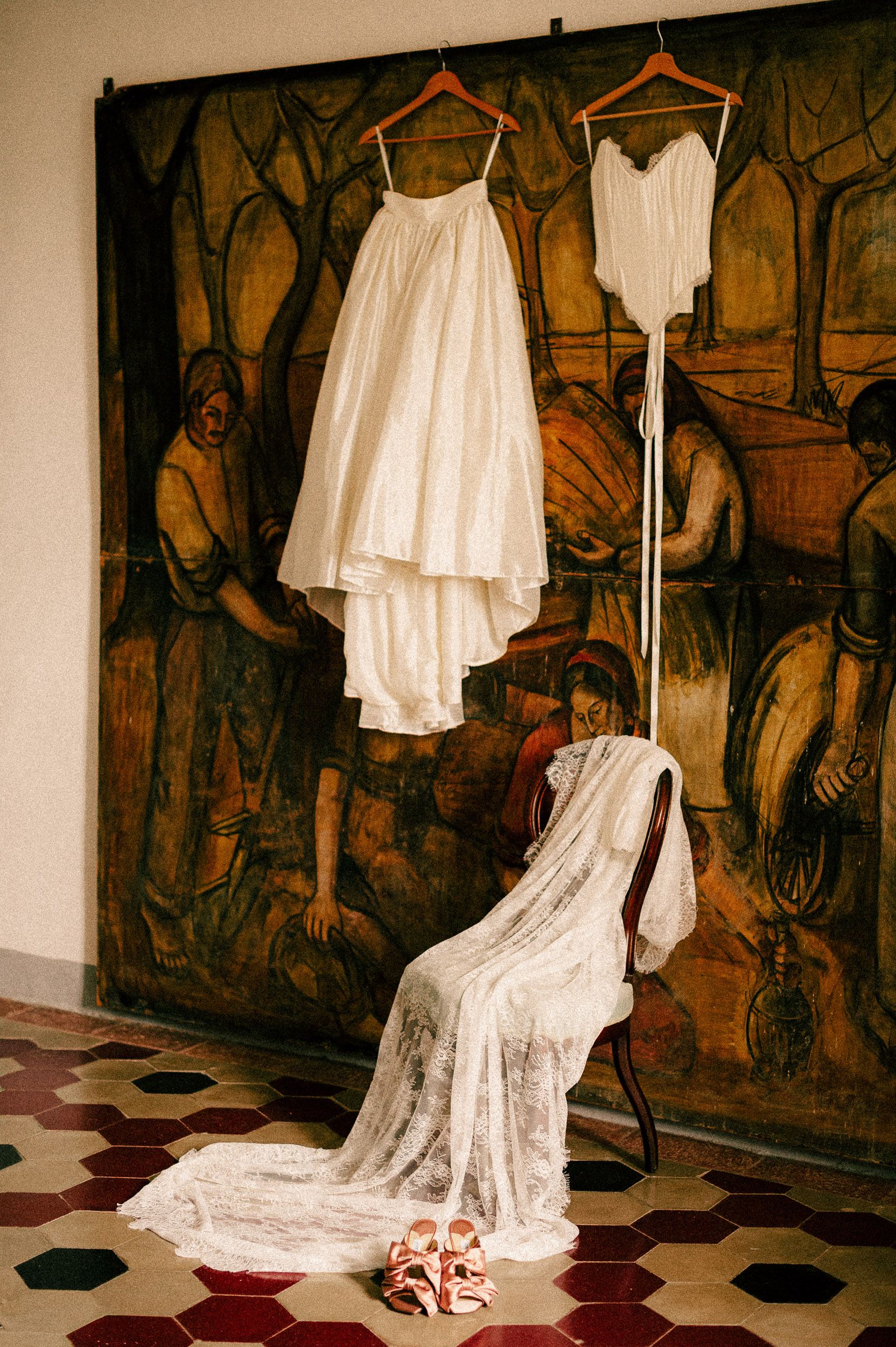 A sequence of white wedding dresses displayed against a dark mural background on tiled floor with red accents.