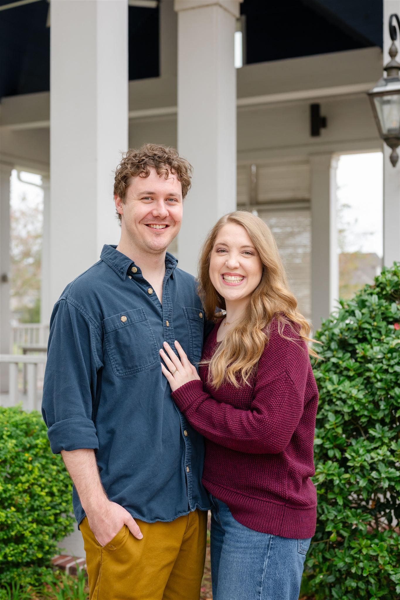 A couple stands together smiling on a porch with white columns in Conroe, texas