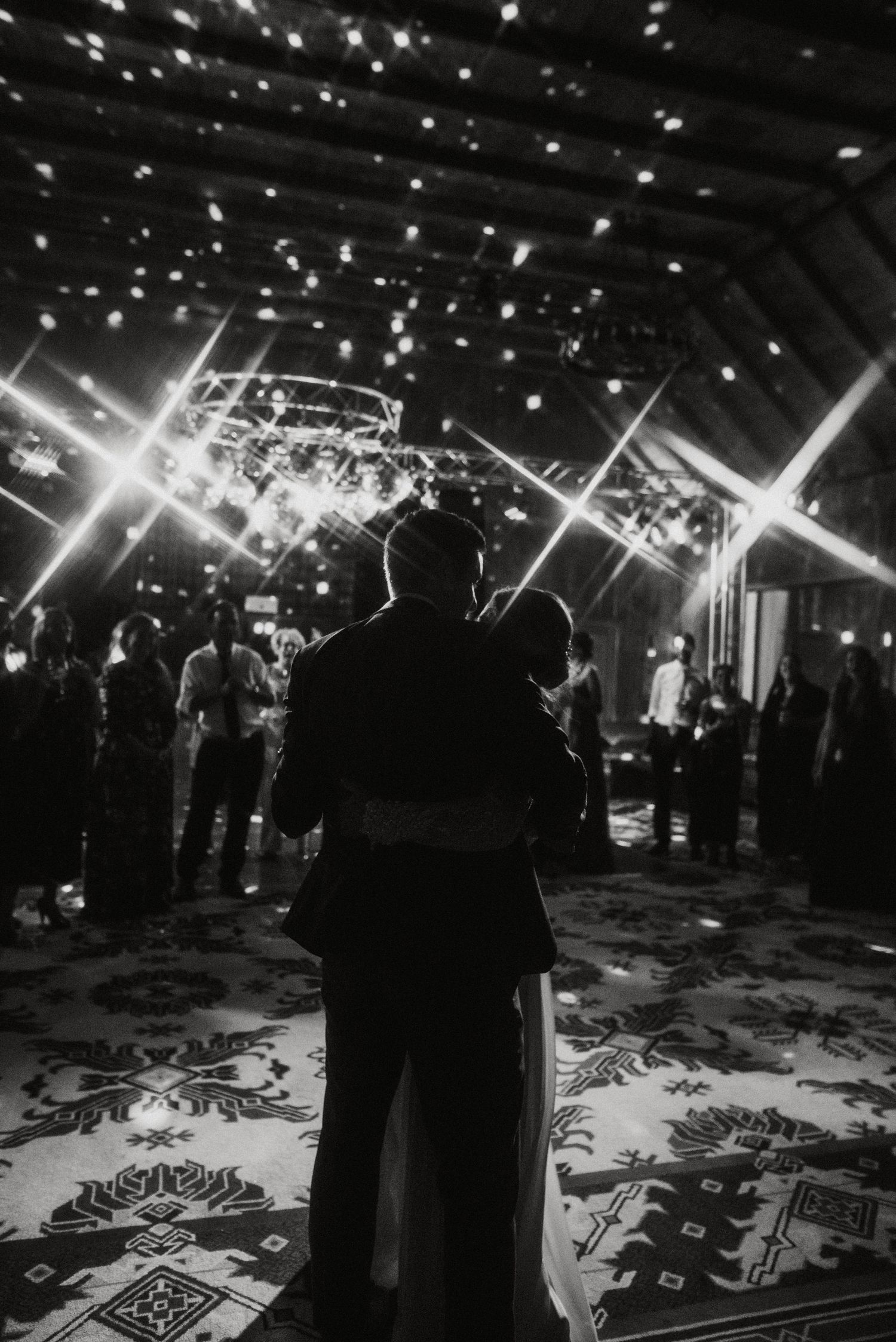 Dancing couple silhouetted under twinkling string lights on patterned dance floor.