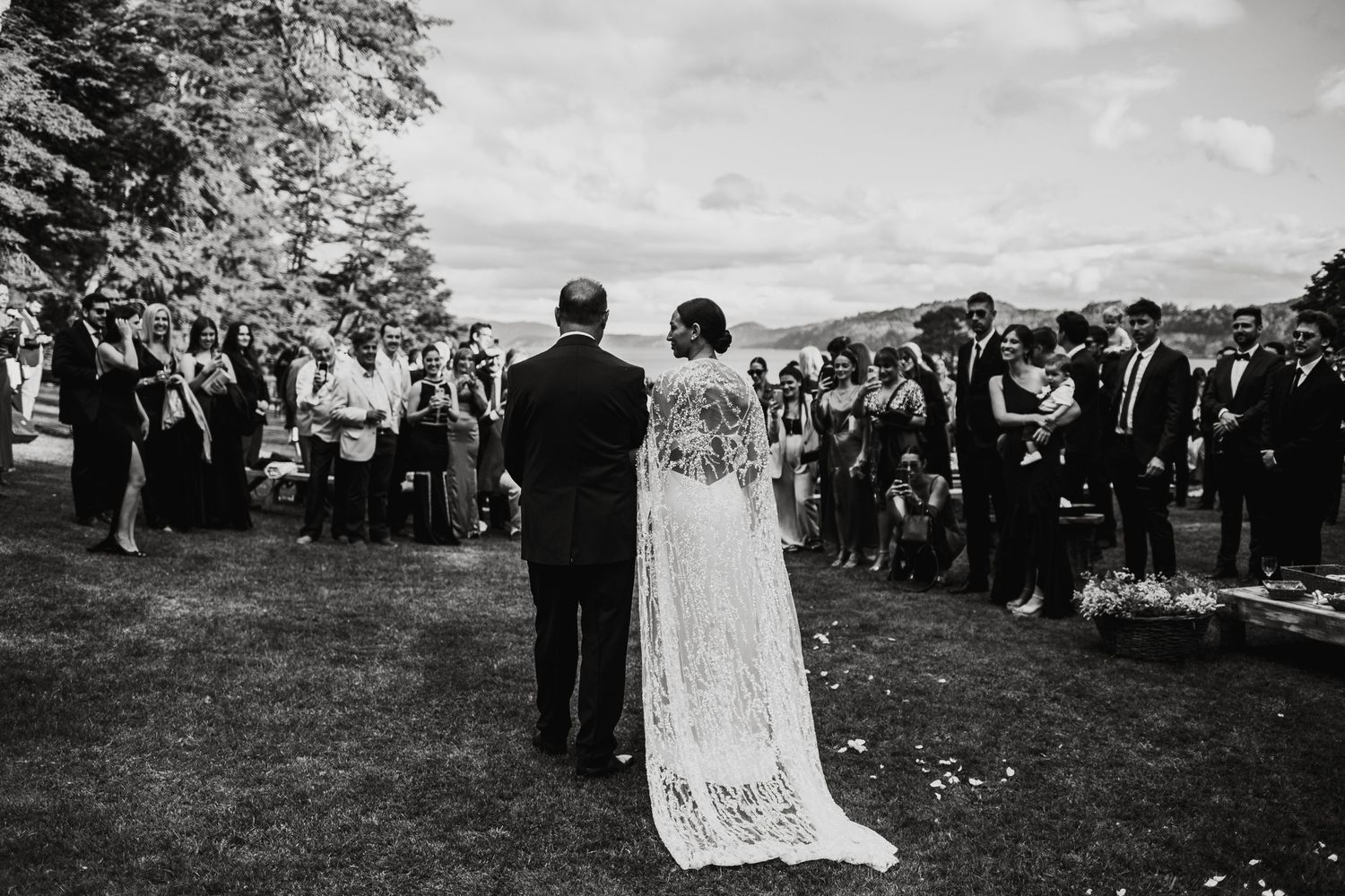 Wide shot of wedding ceremony with guests gathered outdoors among trees.