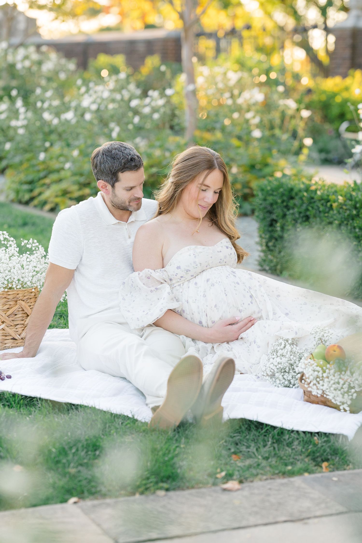 An expecting couple on picnic blanket surrounded by glowing sunlight, fruit, and delicate floral during a maternity session in Pittsburgh.