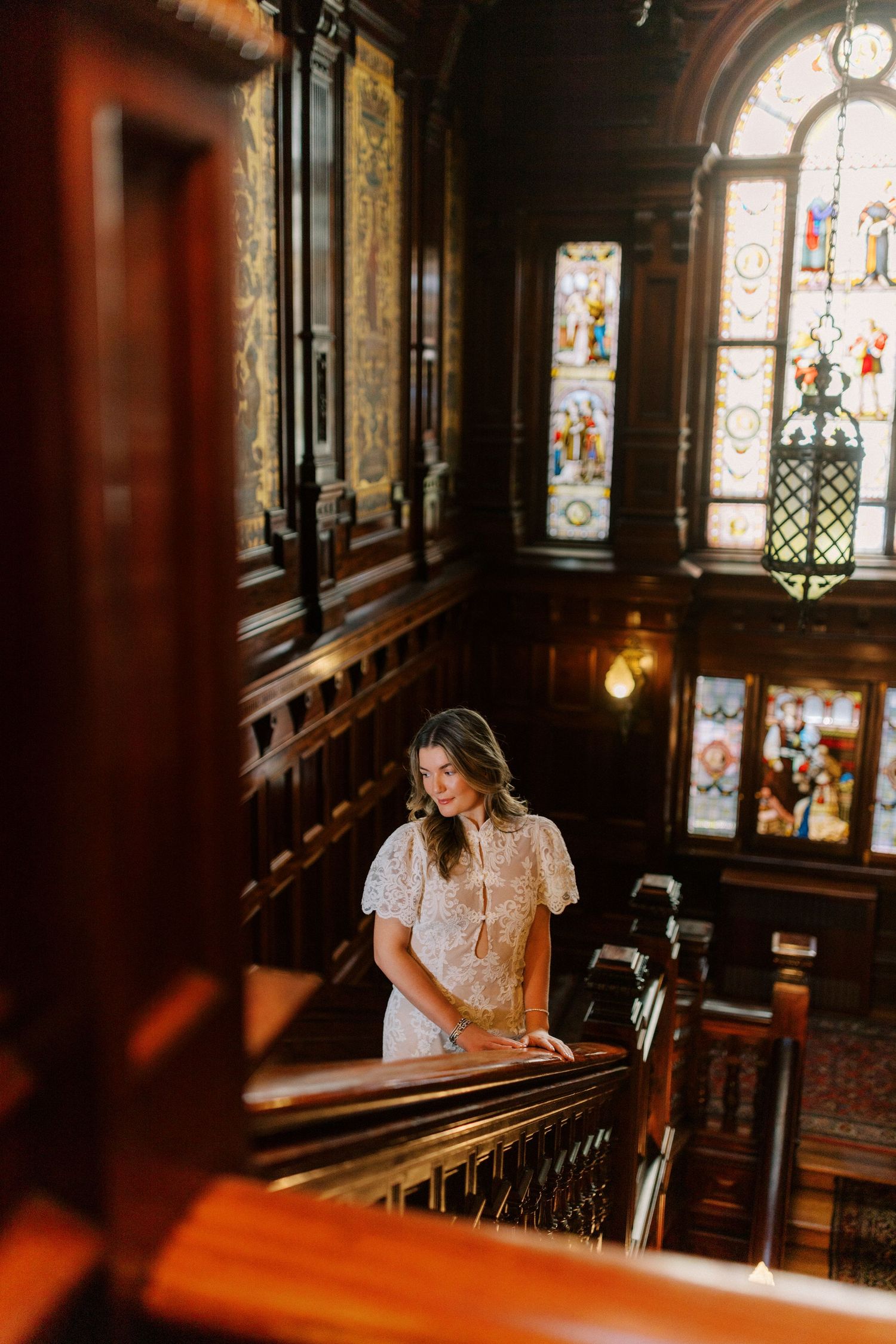 A person in a white dress sits by ornate stained glass windows in a church's wooden interior.