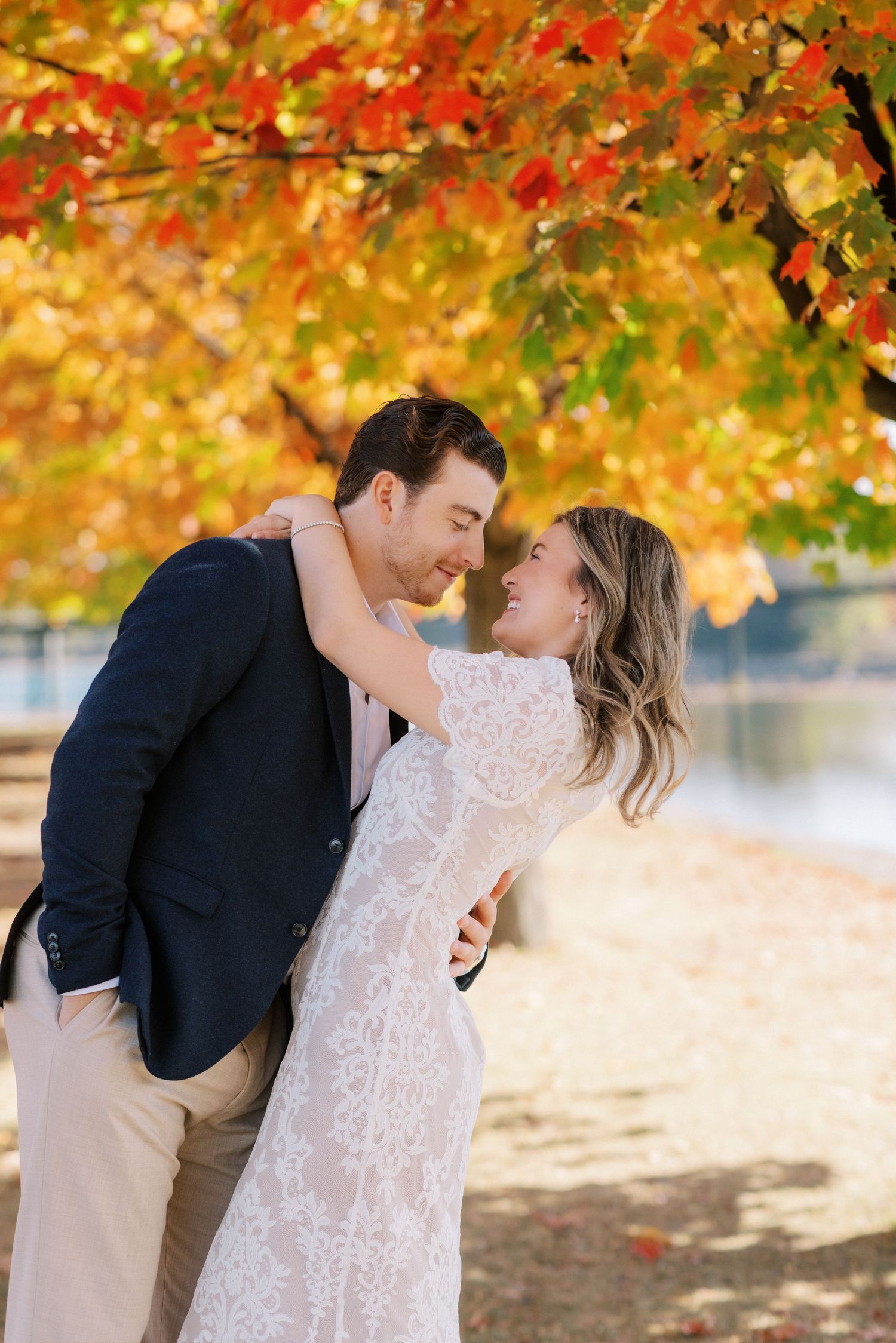 A romantic couple shares a tender moment under vibrant autumn foliage in a park setting.