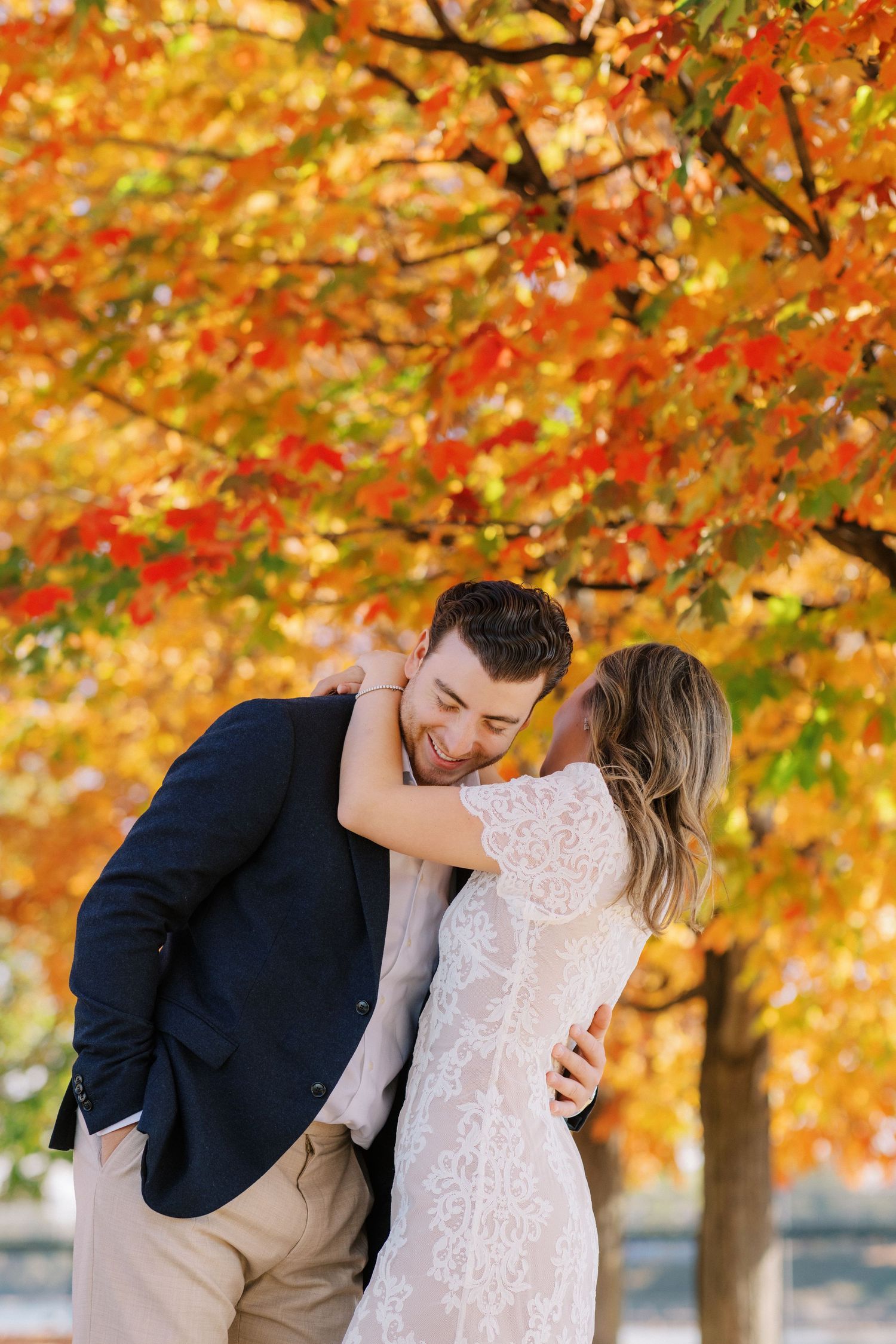 A romantic autumn engagement photo with a couple embracing under vibrant orange and red fall foliage.