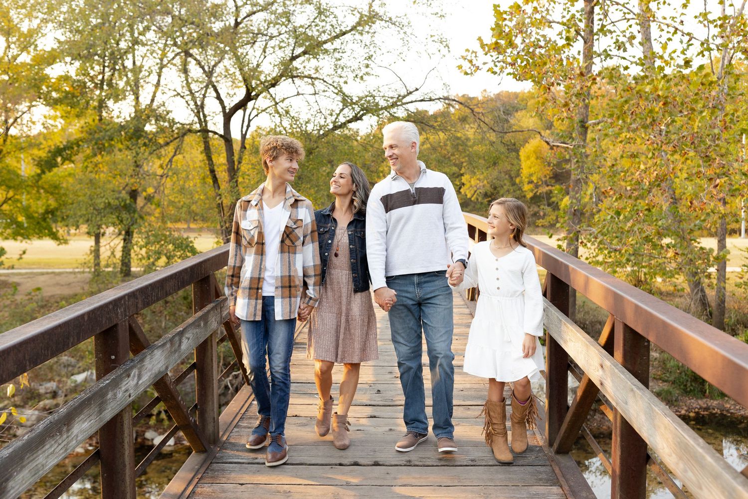 A group walks together on a wooden boardwalk path through autumn trees during a golden sunset.