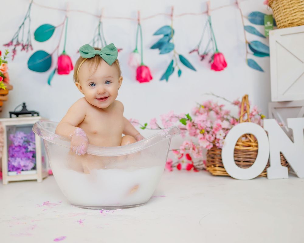 A baby's first birthday cake smash photo session with pink and teal decorations and floral accents.