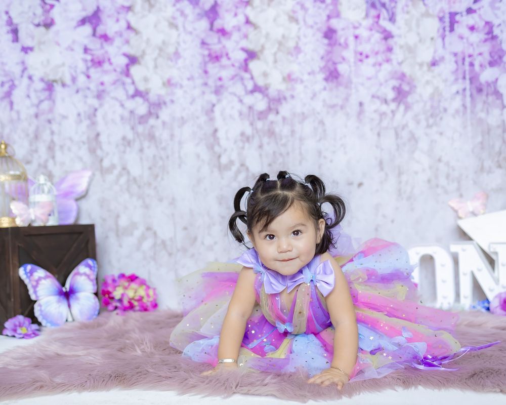 A young child in a colorful fairy costume poses on a white textured backdrop with purple floral accents.