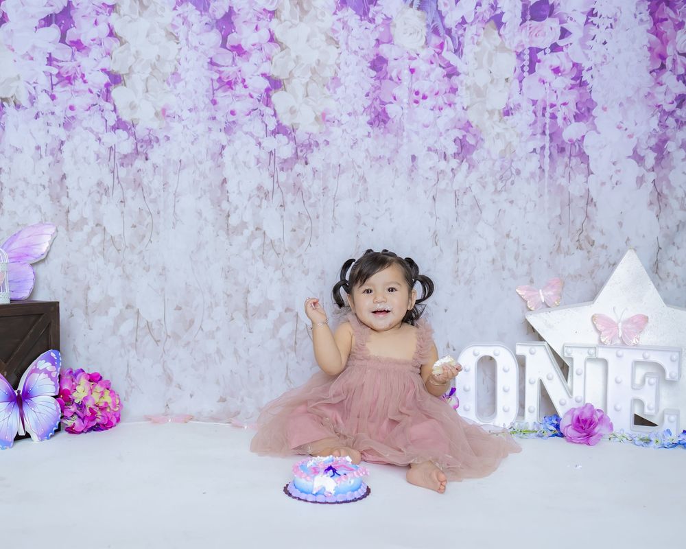 A purple and pink floral backdrop creates a dreamy setting for a birthday celebration with a small cake.