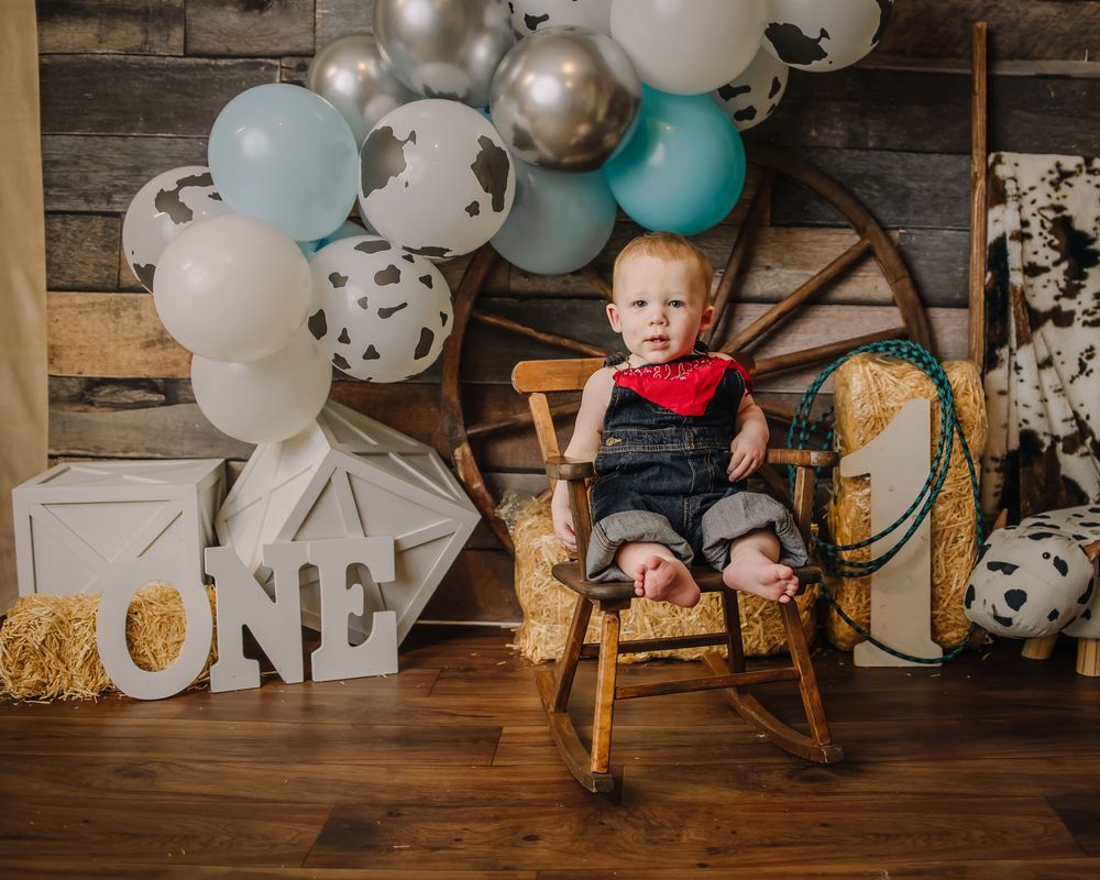 Baby crawls across wooden floor with festive balloons and rustic decor in background.