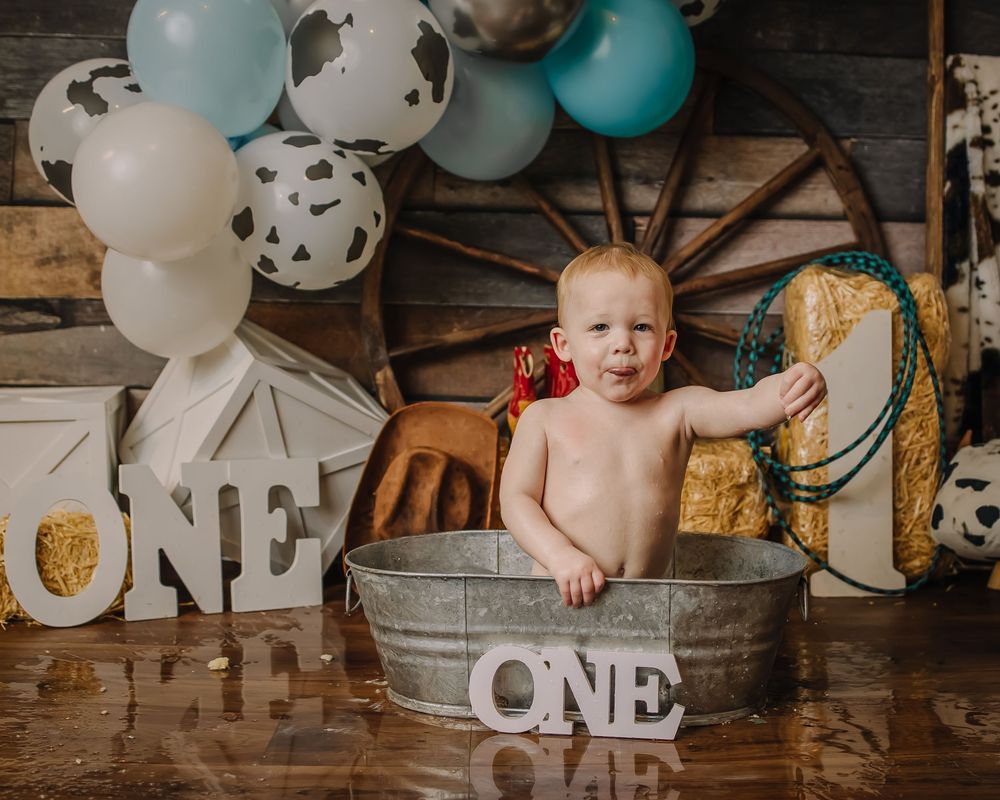 Rustic farmhouse birthday setup with galvanized tub, 'ONE' letters, and balloon garland.