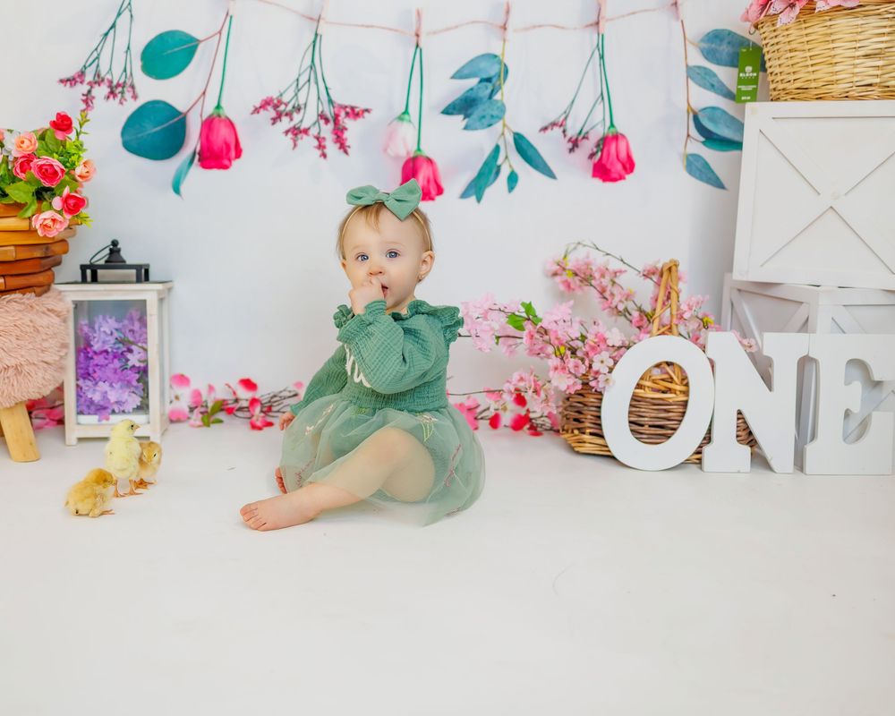 Decorative party setup with floral garland, pink and teal accents against white backdrop with ONE sign.