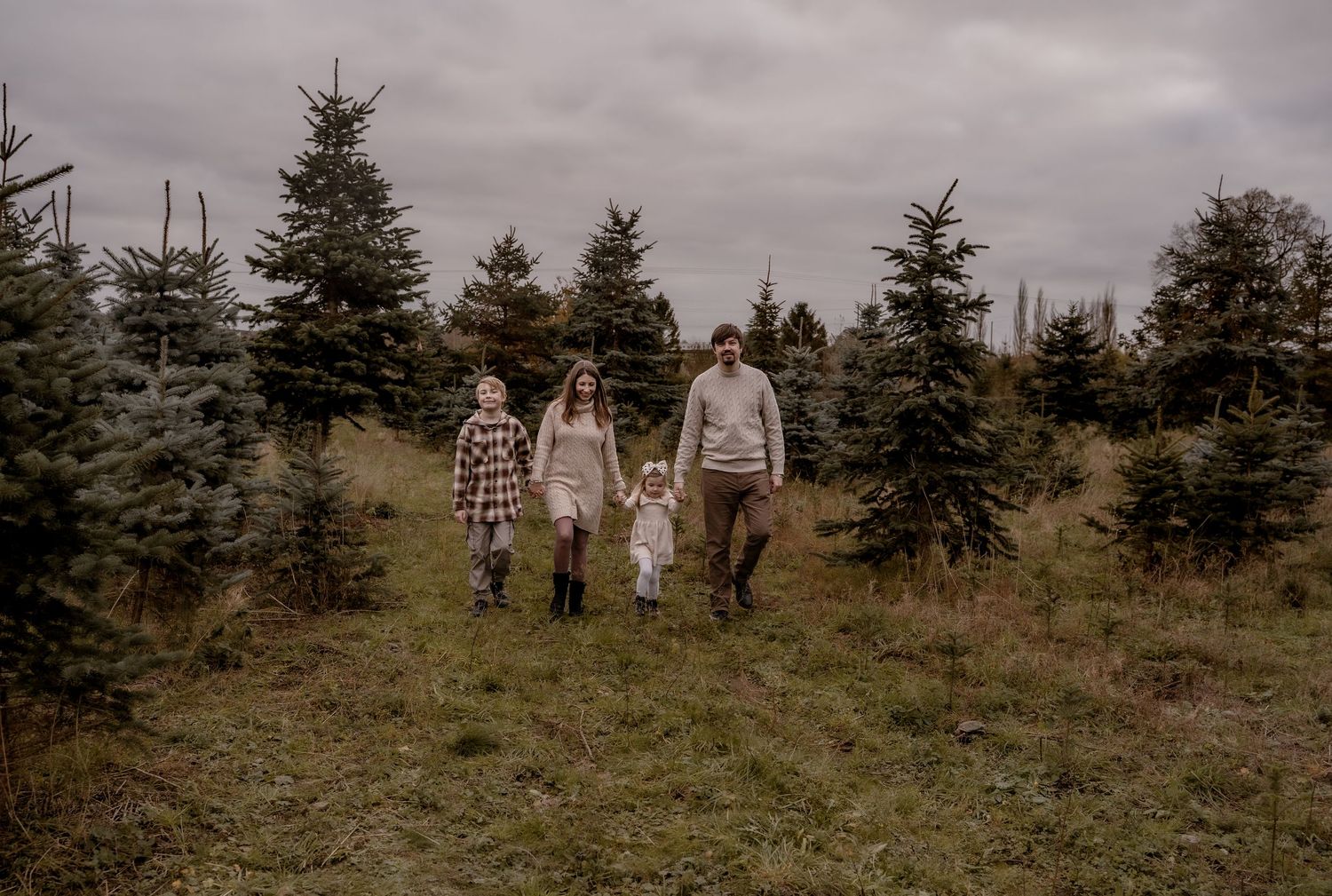 A family walks together through an evergreen tree farm on an overcast WINTER DAYS