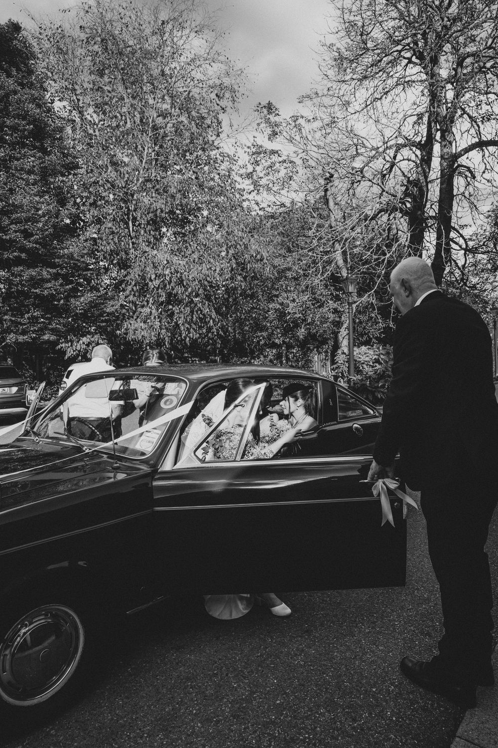Classic vintage car parked on grass with trees in background during what appears to be a formal event.