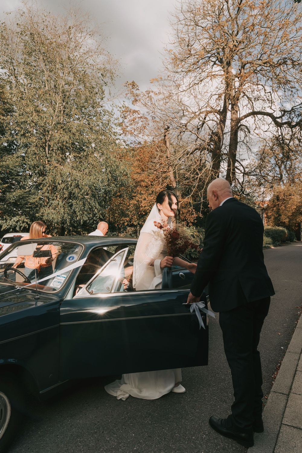 Wedding couple getting into a classic black vintage car after their ceremony.
