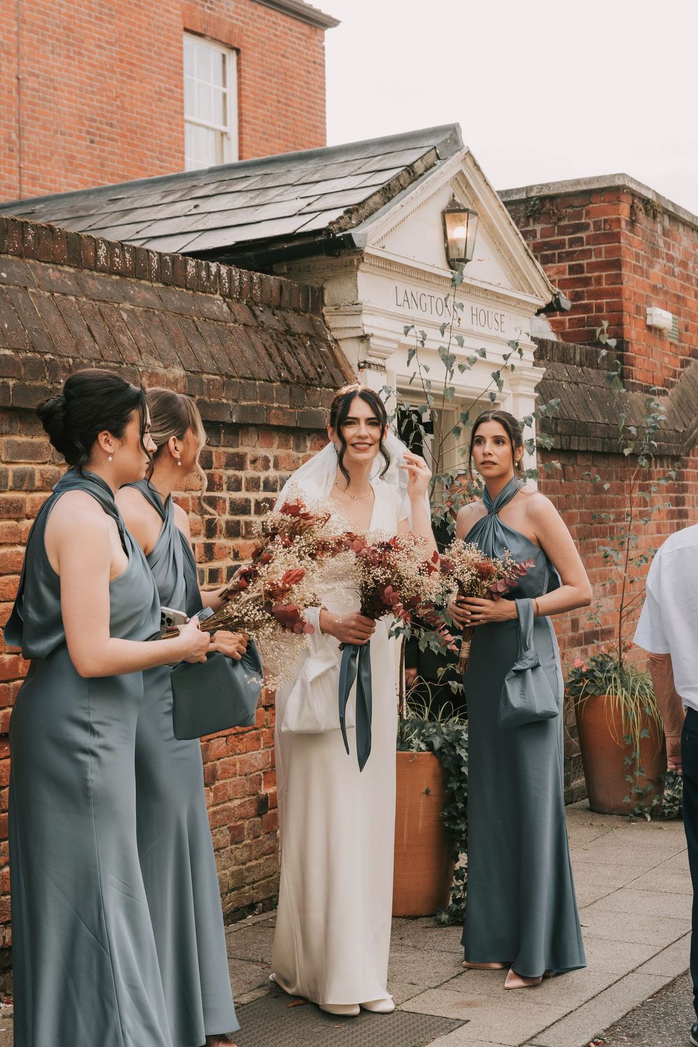 A wedding party in blue dresses gathered outside a historic brick building.