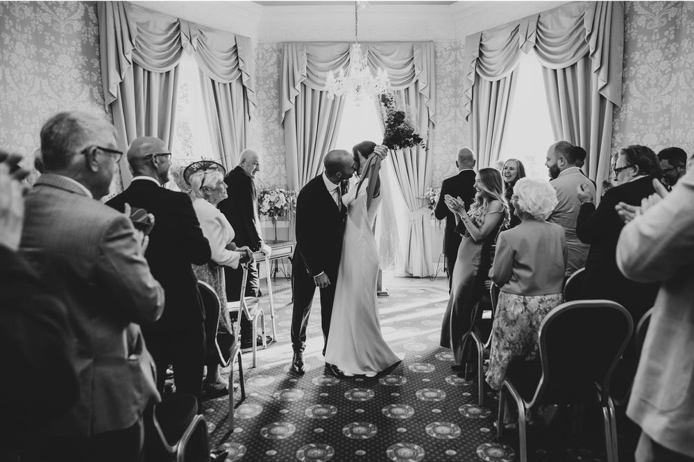 Wedding guests gather in an elegant ballroom with draped curtains and ornate decor for a formal celebration.