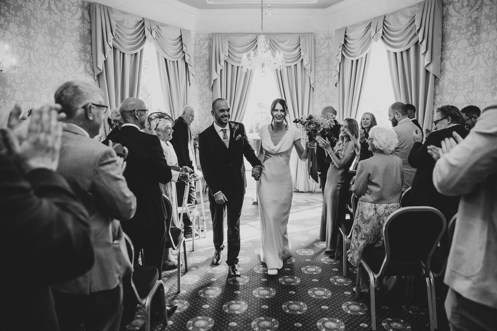 Black and white wedding ceremony photos show a sequence of joyful moments with guests and the wedding party in an elegant venue.