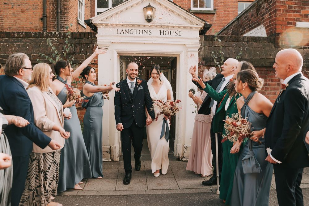 Wedding guests form a celebratory exit line outside a brick building with a lantern at sunset.