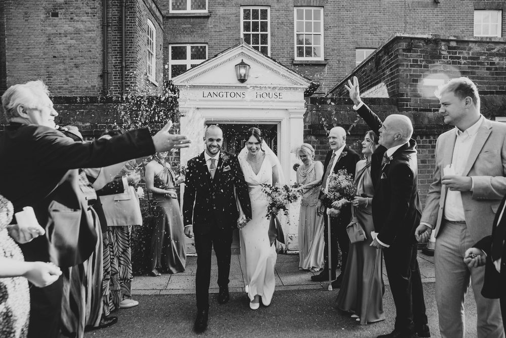 Wedding guests gathered outside a historic brick building throwing confetti in celebration.