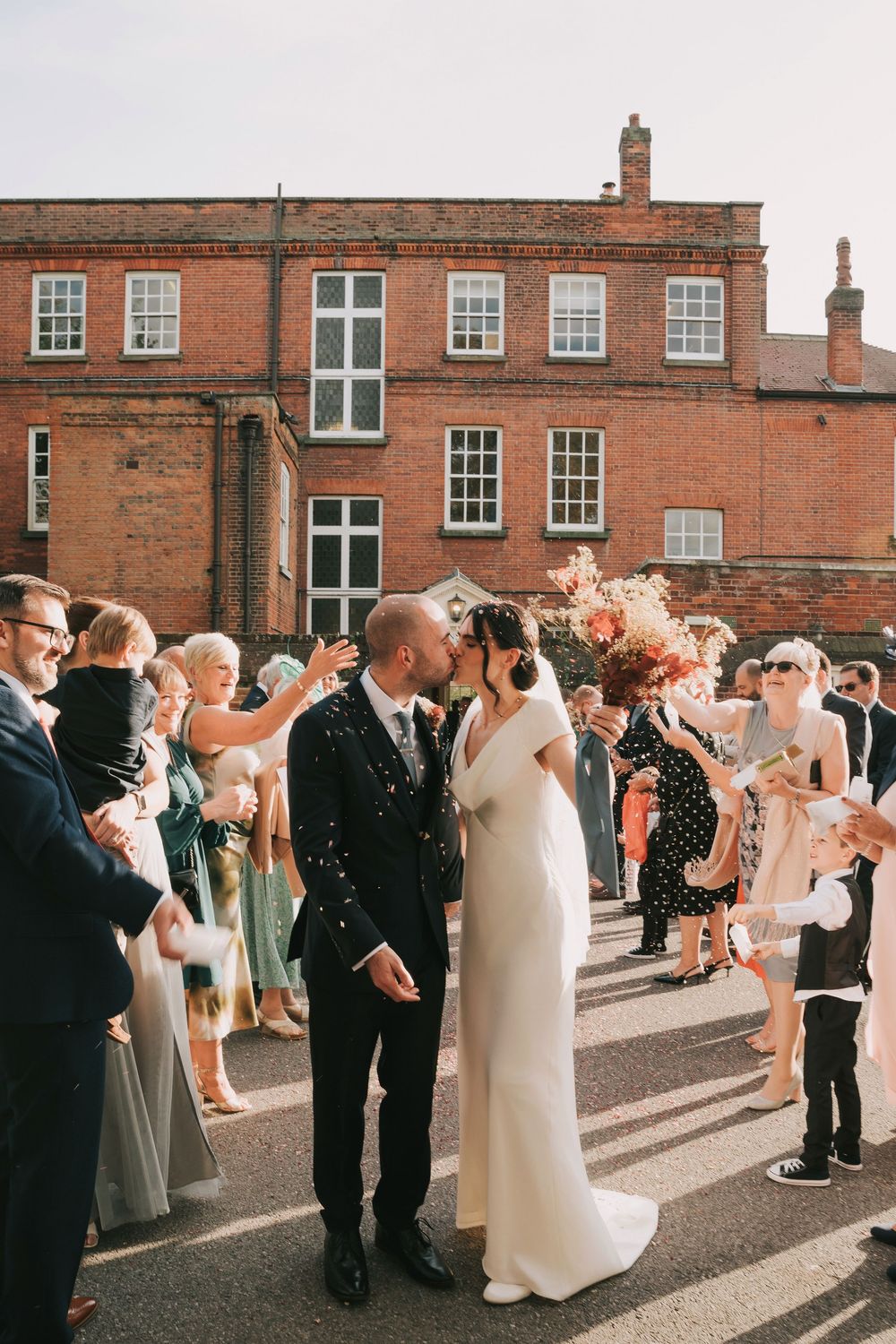 Guests line up along a brick building's exterior to celebrate the newlyweds with confetti.