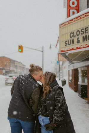 A couple shares an intimate moment in the snow outside a theater.