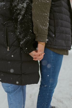 Close-up of two people holding hands while wearing winter coats in the snow.
