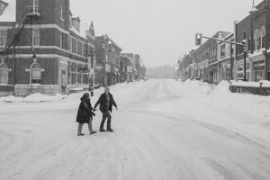Two people walk together down a snow-covered historic street.