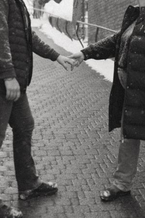 Two people holding hands while standing on a cobblestone street in black and white.