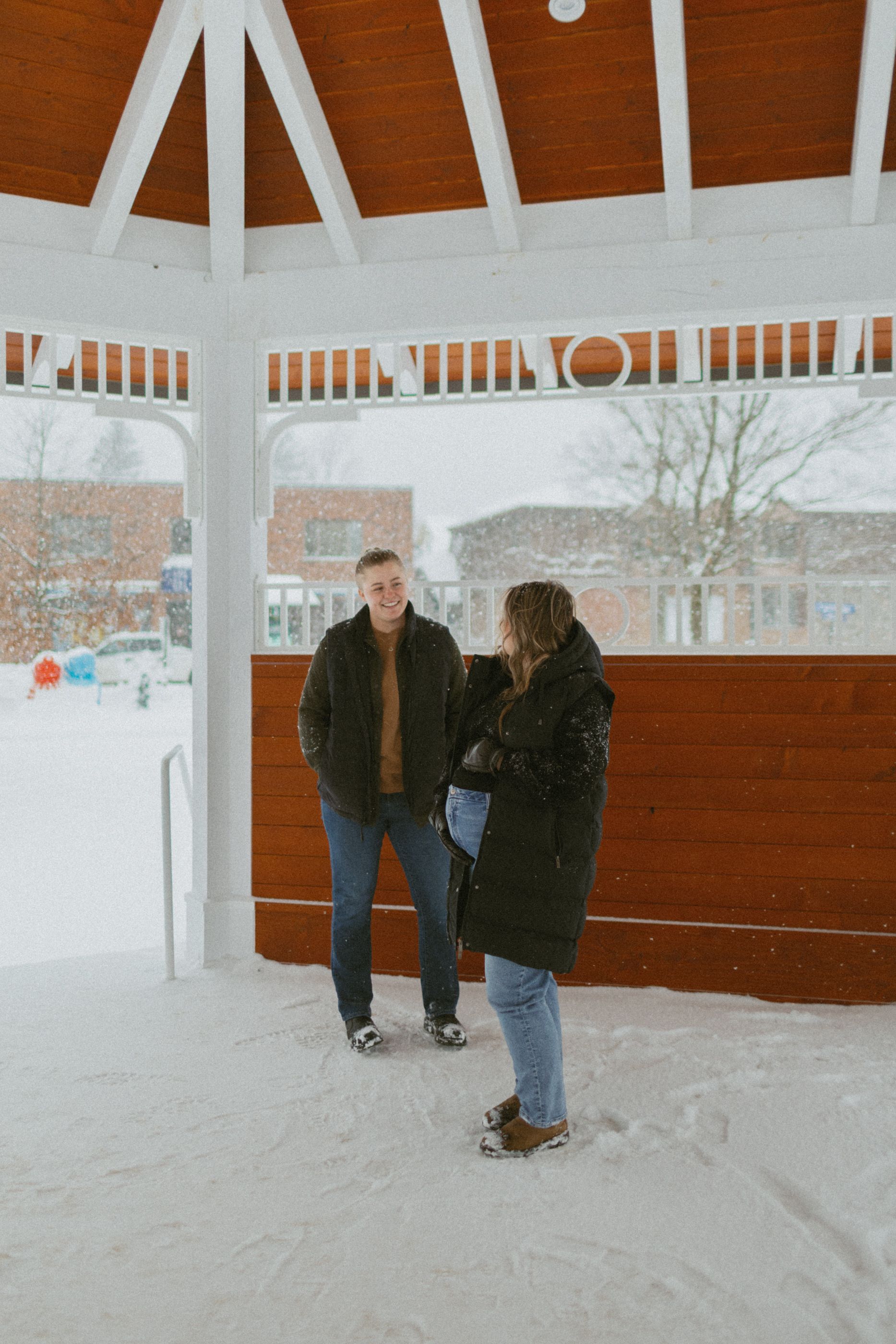 A couple stands together in a snowy gazebo on a winter day.