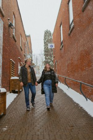A couple walking hand in hand down a snowy brick alleyway.