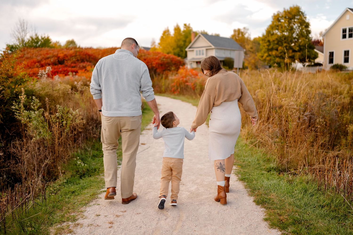 A family walks together on a scenic autumn path surrounded by fall foliage and rural homes.